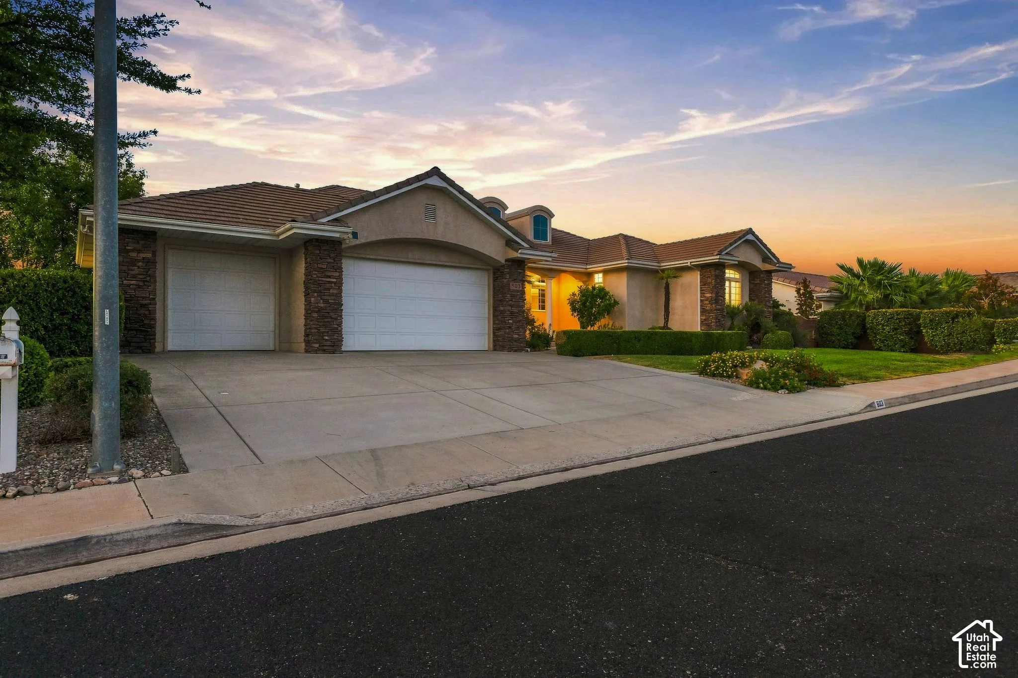 Stucco exterior with stone accents, a tile roof, two garage doors, and a concrete driveway