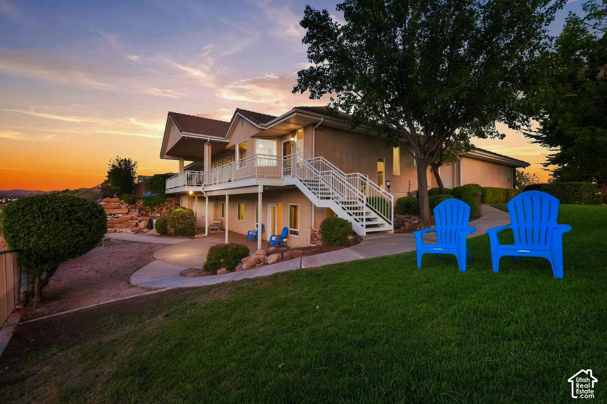 Multi-level exterior with balconies, featuring a concrete patio, landscaped rock gardens, and a sloped lawn