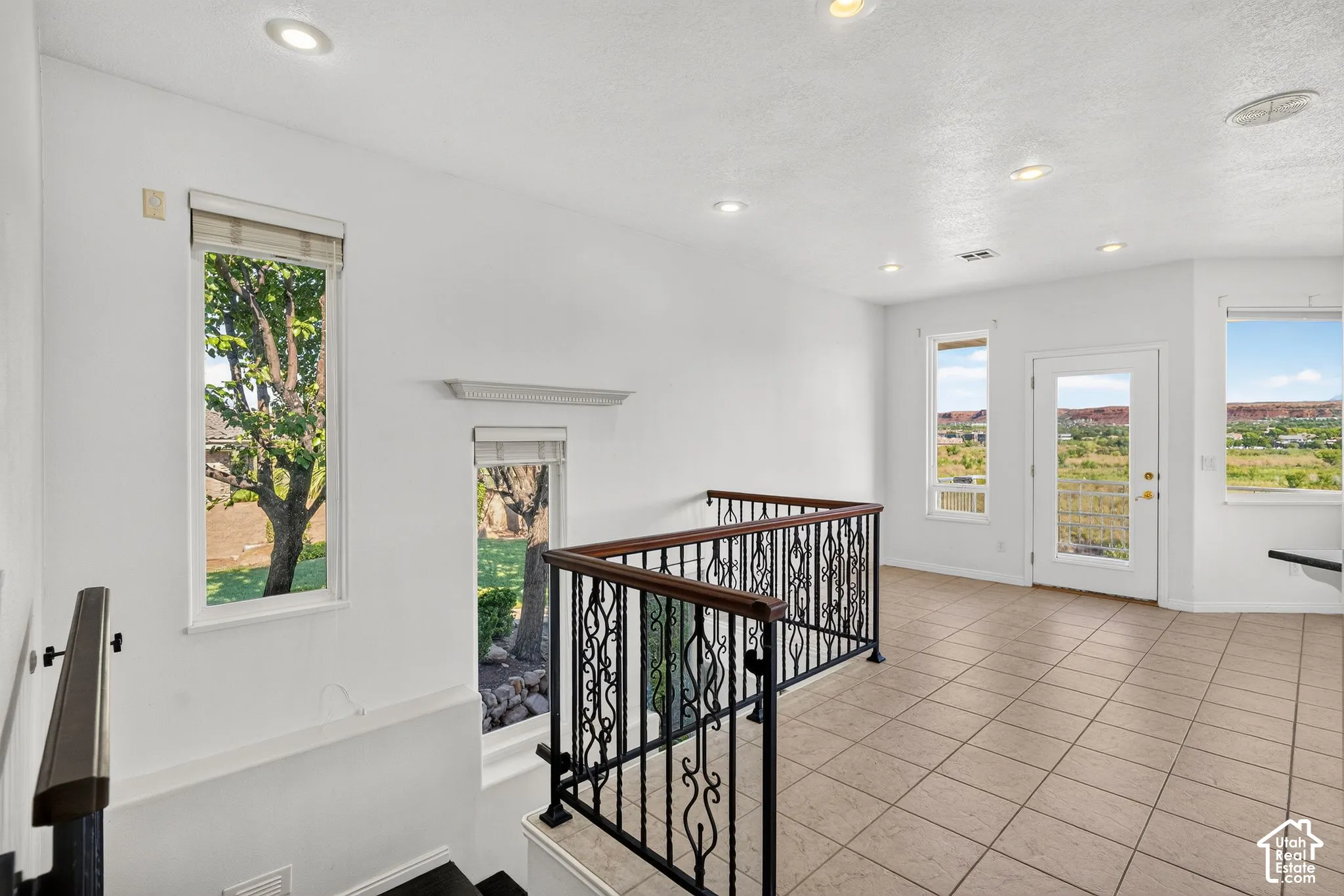 Upper landing featuring tile flooring, wrought iron railing with wood handrails, recessed lighting, and multiple windows