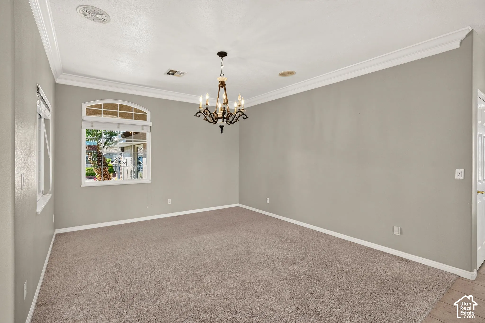 Spacious room featuring neutral wall finishes, pristine white crown molding and trim, plush carpeting, recessed ceiling lighting, and an elegant chandelier fixture overhead