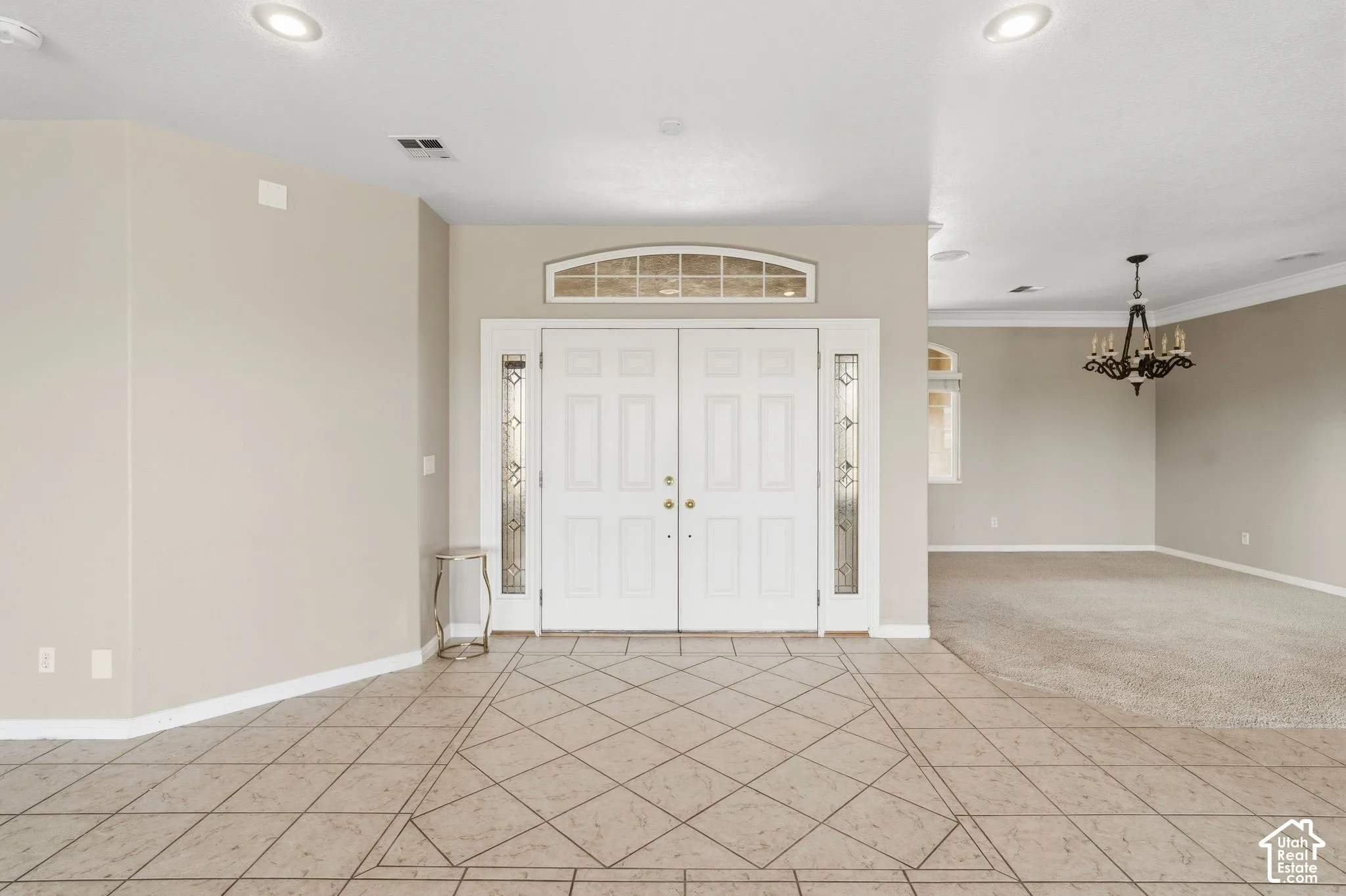 Elegant foyer showcasing double French doors with transom window, sidelights, and polished tile flooring laid in a geometric diamond pattern