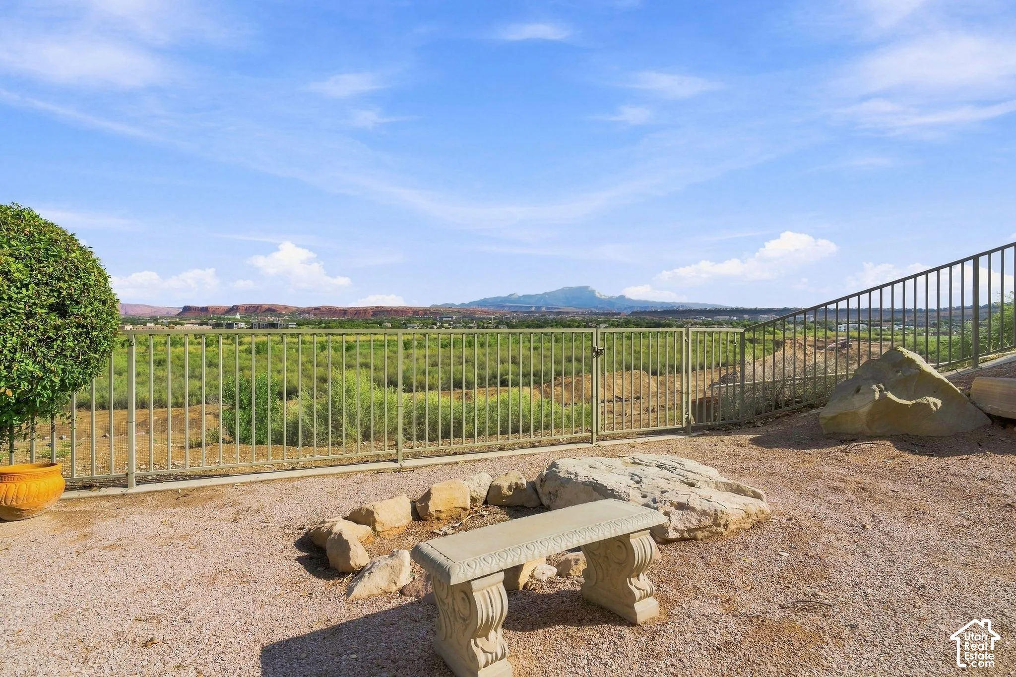 Gravel patio featuring a stone bench, fire pit area with natural rock surround, and metal fencing