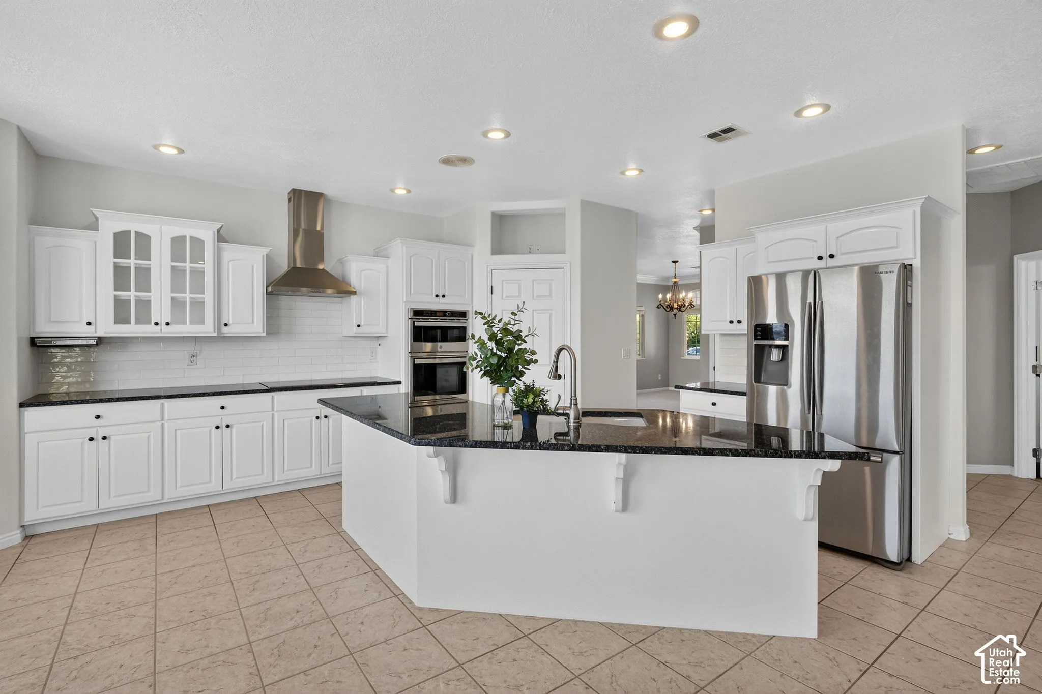 Chef's kitchen featuring white cabinetry with glass-front uppers, stainless steel appliances including double wall ovens and a professional-style range hood, quartz countertops, a large center island with seating, recessed ceiling lighting, and tile floor