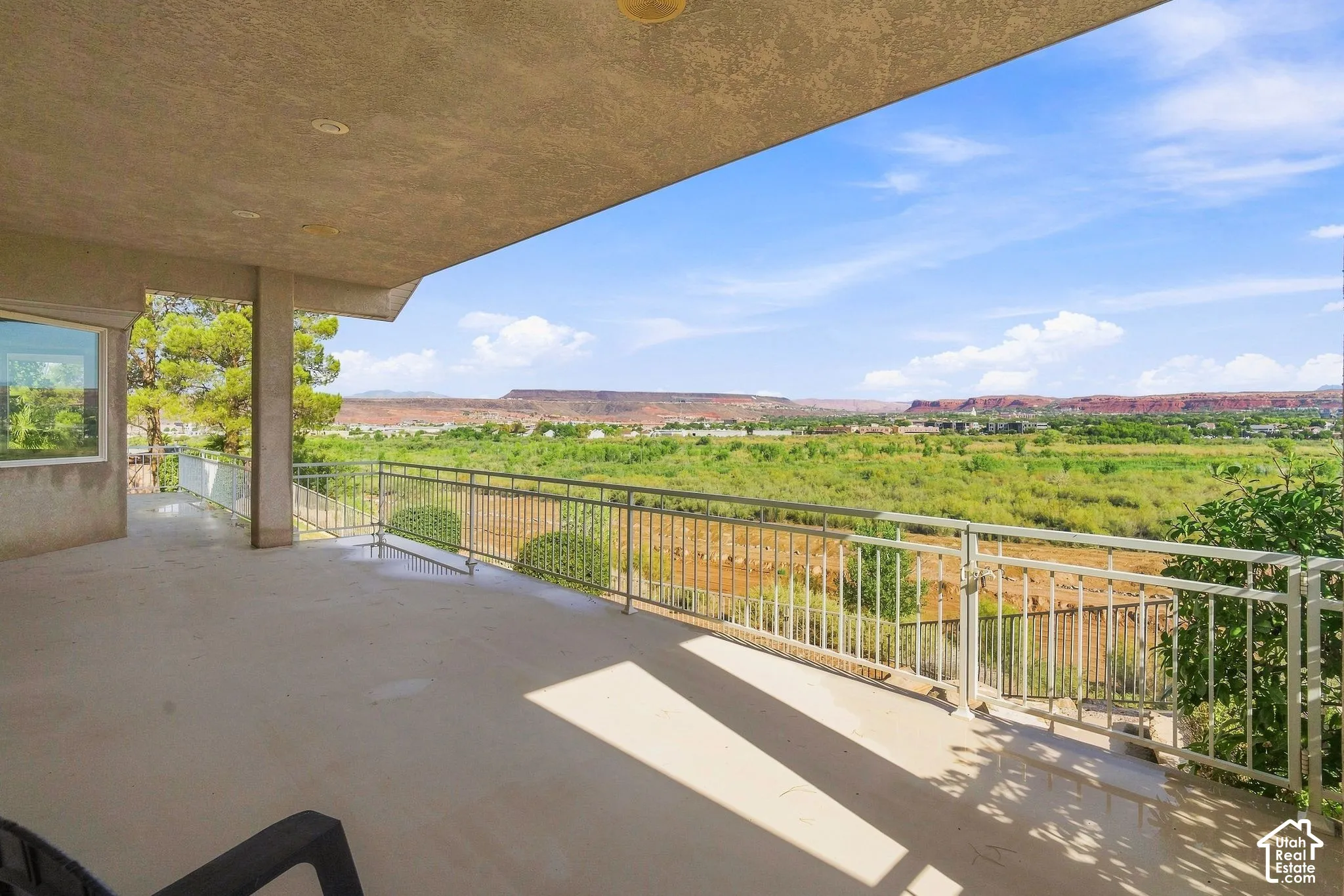 Expansive outdoor balcony with metal railing, offering a scenic backdrop of verdant plains and distant red rock formations