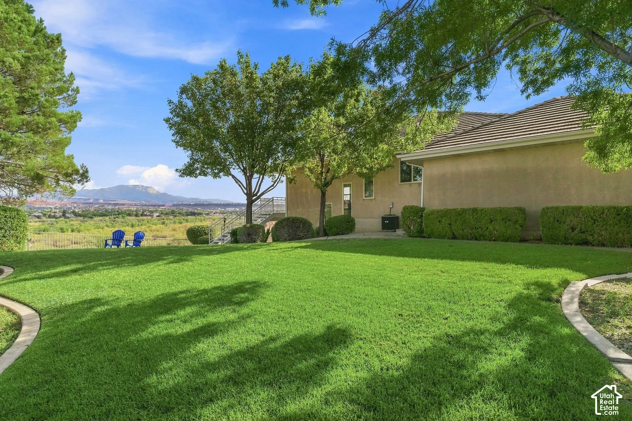 Expansive lawn with concrete curbing, mature trees, and stucco exterior