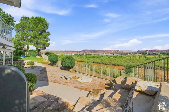 Expansive outdoor entertaining space featuring a concrete patio with natural stone accents, wrought iron railings, and manicured landscaping with mature trees and boxwood hedges
