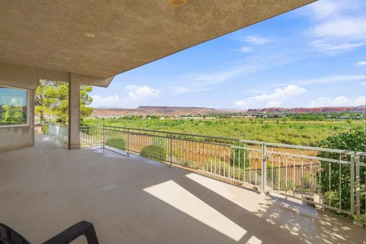 Expansive outdoor balcony with metal railing, offering a scenic backdrop of verdant plains and distant red rock formations
