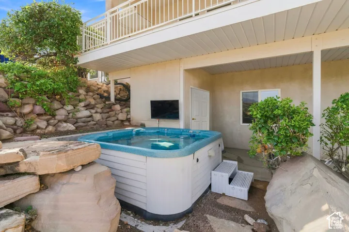 Covered patio featuring a relaxing hot tub with integrated jets, surrounded by mature landscaping and stone accents