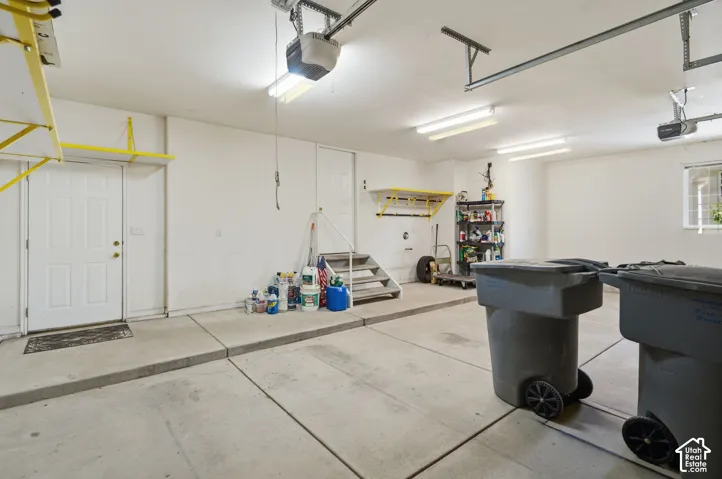 Attached two-car garage with concrete flooring, multiple overhead fluorescent light fixtures, and an automatic garage door opener