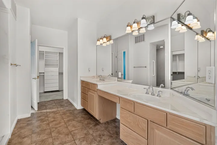 Dual vanity with integrated sinks, light wood-finish cabinetry, and expansive wall-mounted mirrors