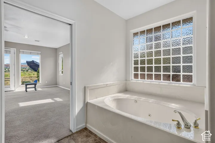 Jetted tub with a stone surround, glass block window, and dual-tone fixtures