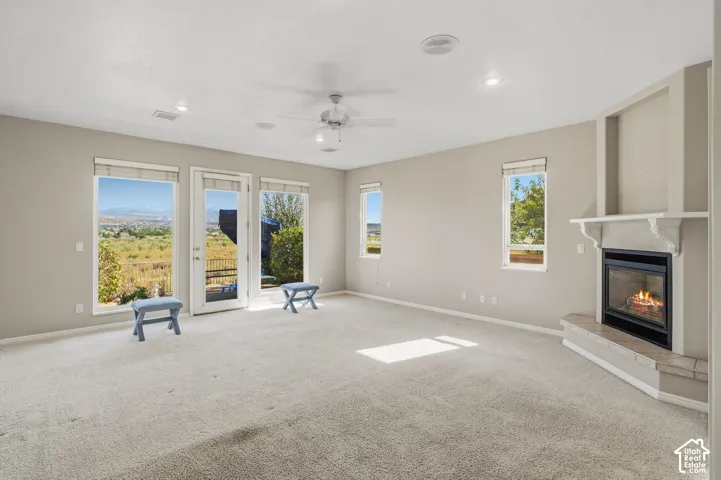 Expansive great room bathed in natural light through multiple French doors and windows, showcasing neutral carpet flooring, a ceiling fan with recessed lighting, and a gas fireplace with a light-finish surround