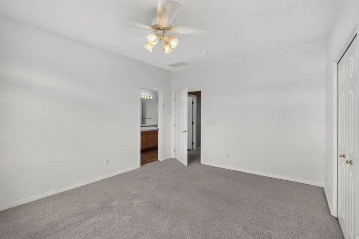 Spacious bedroom with neutral carpet flooring, ceiling fan with integrated lighting, and multiple closet access points