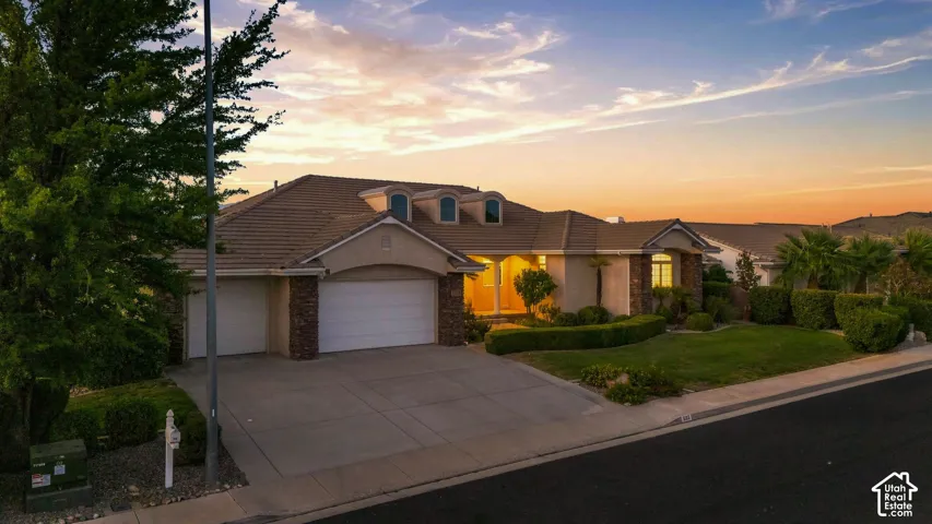 Sleek roofline with dormer windows, stone accent facade, two-car garage, manicured lawn, and mature landscaping