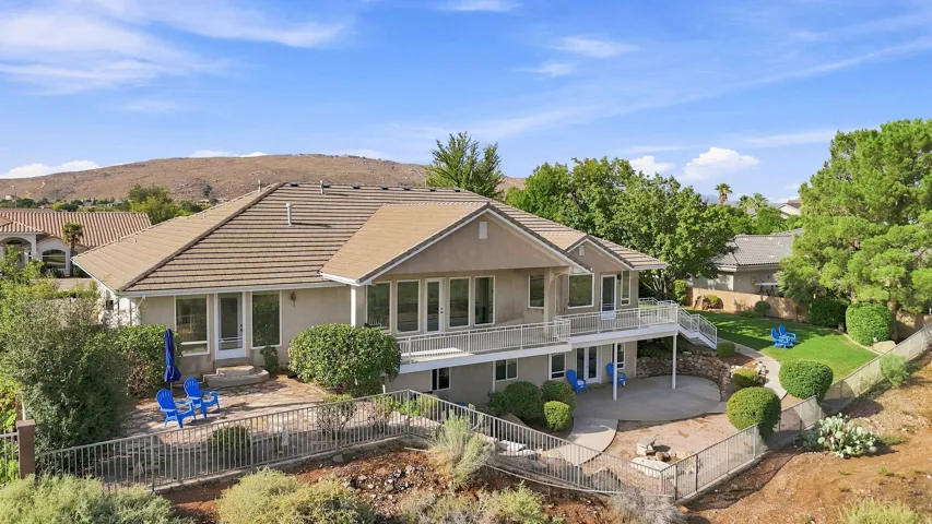 Terracotta tile roof, multiple outdoor patios, upper-level balcony with white railings, and a terraced landscaped yard
