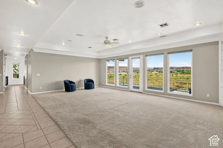 Spacious room featuring a tray ceiling, recessed lighting, ceiling fan, and extensive windows with outdoor access