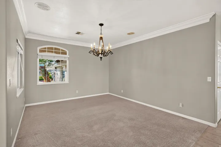 Spacious room featuring neutral wall finishes, pristine white crown molding and trim, plush carpeting, recessed ceiling lighting, and an elegant chandelier fixture overhead