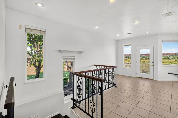 Upper landing featuring tile flooring, wrought iron railing with wood handrails, recessed lighting, and multiple windows