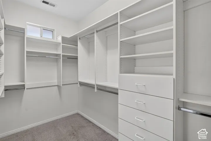 Spacious walk-in closet featuring custom built-in shelving and hanging rods throughout, four drawers with metal hardware, and polished concrete flooring