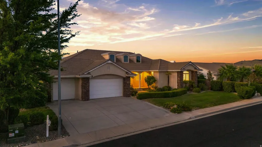 Sleek roofline with dormer windows, stone accent facade, two-car garage, manicured lawn, and mature landscaping