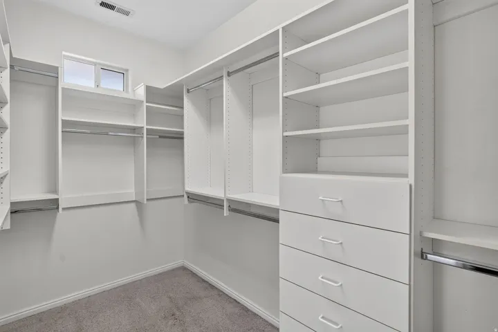 Spacious walk-in closet featuring custom built-in shelving and hanging rods throughout, four drawers with metal hardware, and polished concrete flooring