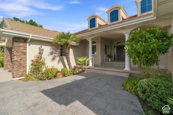 Stamped concrete driveway, stone column accents, covered entry with columns, arched dormer windows, and mature landscaping