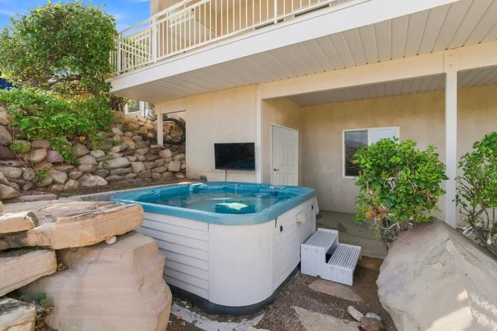 Covered patio featuring a relaxing hot tub with integrated jets, surrounded by mature landscaping and stone accents