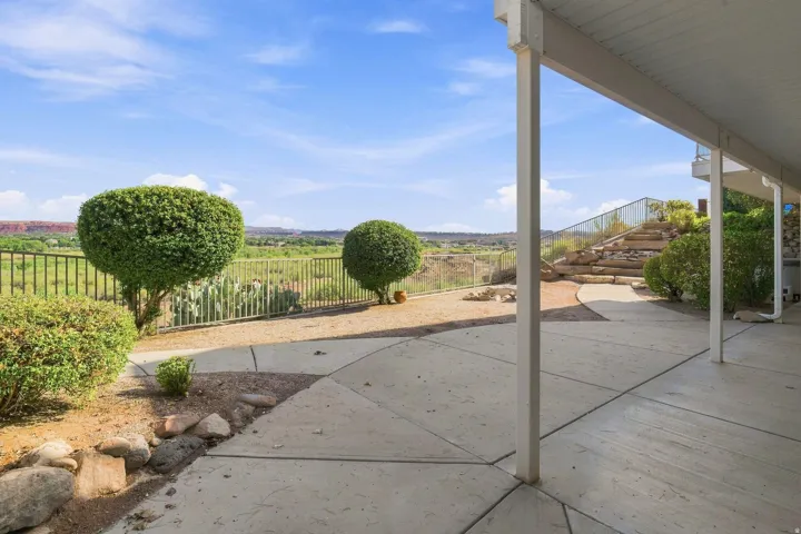 Expansive concrete patio with a covered outdoor area, terraced landscaping, metal fencing, and established shrubbery