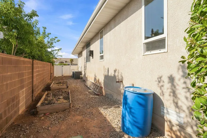 Stucco exterior with multiple windows, concrete block wall, raised garden beds, and gravel landscaping