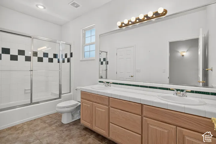 Dual vanity with white tile countertop, extensive wall mirror, and integrated lighting fixture