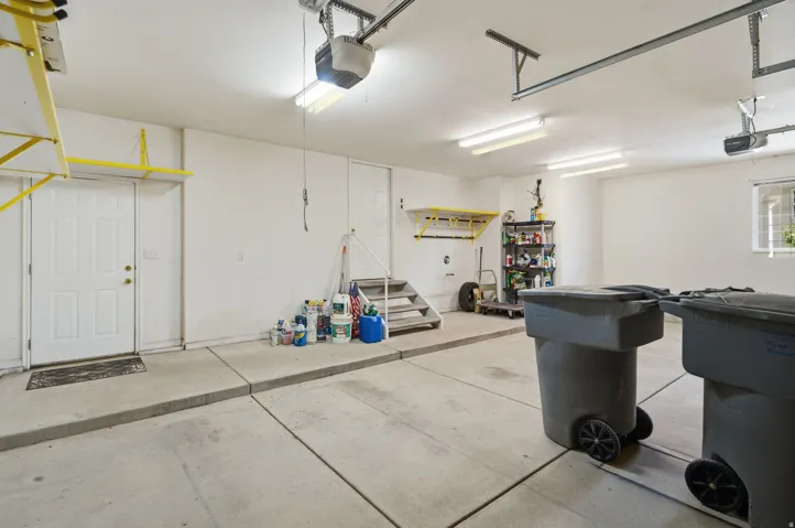 Attached two-car garage with concrete flooring, multiple overhead fluorescent light fixtures, and an automatic garage door opener