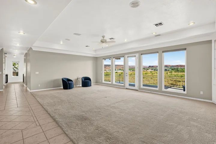 Spacious room featuring a tray ceiling, recessed lighting, ceiling fan, and extensive windows with outdoor access