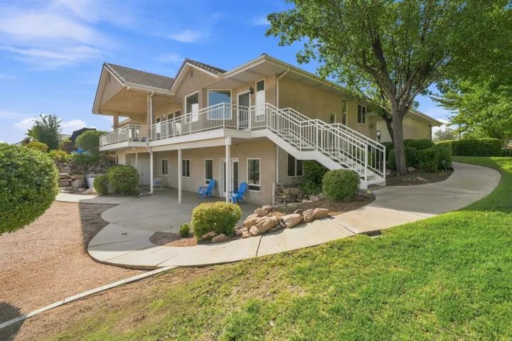 Elegant two-story residence featuring a taupe exterior with peaked rooflines and expansive front-facing deck with metal railings