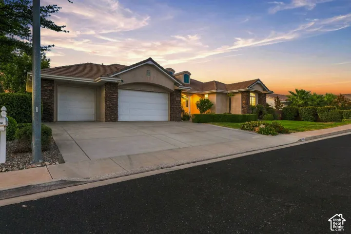 Stucco exterior with stone accents, a tile roof, two garage doors, and a concrete driveway