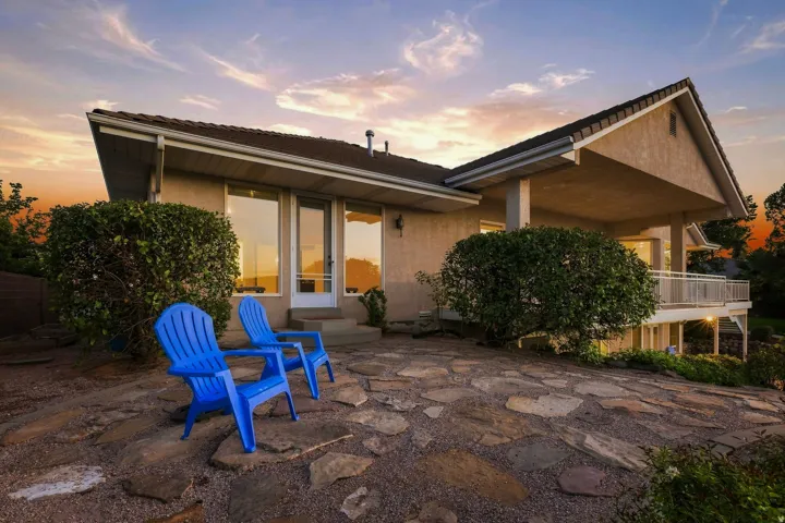 Exterior stucco finish, prominent gabled roof, flagstone patio, covered balcony, and mature landscaping