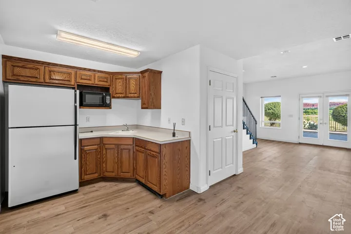 Open-concept living area with wood-finish flooring throughout, featuring a compact kitchenette with wood cabinetry, white appliances, and stainless steel sink