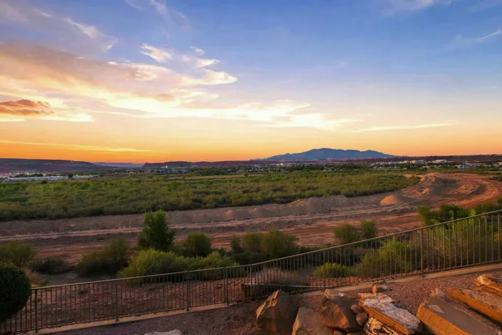 Expansive desert landscape with distant mountains, mature low-lying vegetation, and a metal perimeter fence