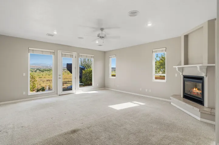 Spacious room with light-colored carpeting, multiple windows providing expansive scenery, a built-in fireplace with a mantel, and recessed ceiling lighting