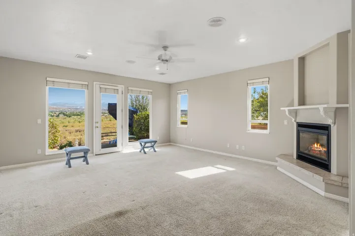 Expansive great room bathed in natural light through multiple French doors and windows, showcasing neutral carpet flooring, a ceiling fan with recessed lighting, and a gas fireplace with a light-finish surround