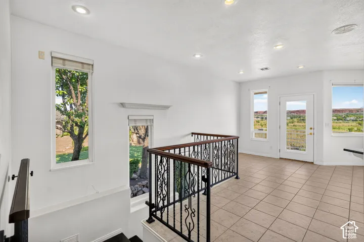 Upper landing featuring tile flooring, wrought iron railing with wood handrails, recessed lighting, and multiple windows