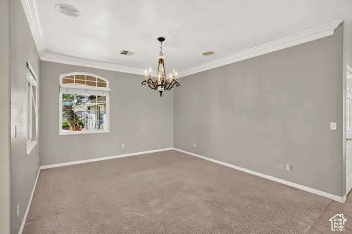 Spacious room featuring neutral wall finishes, pristine white crown molding and trim, plush carpeting, recessed ceiling lighting, and an elegant chandelier fixture overhead