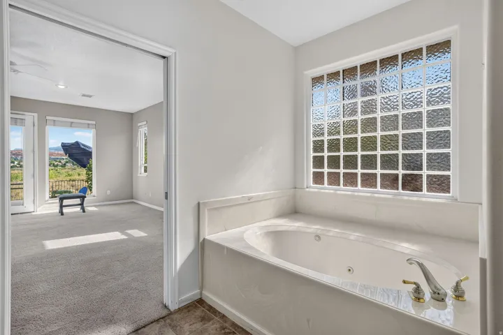 Jetted tub with a stone surround, glass block window, and dual-tone fixtures