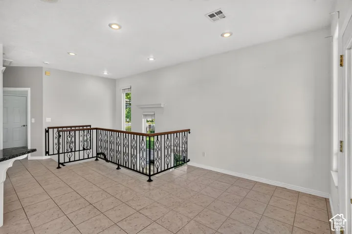 Tiled flooring, wrought iron railing with wood-finish top, recessed lighting, and a white interior door