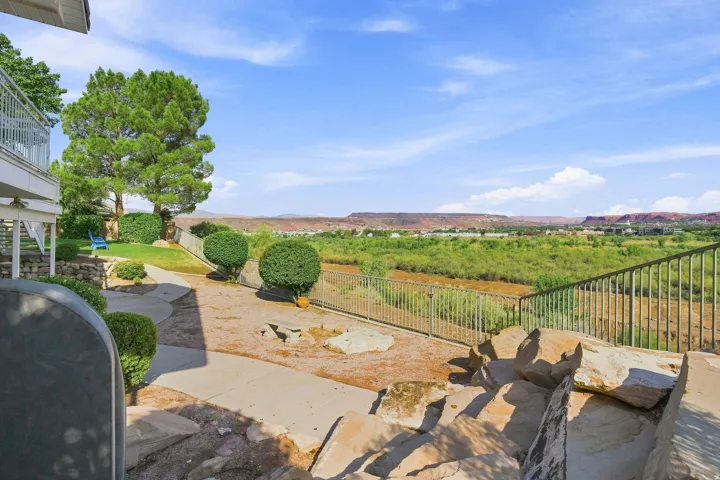 Expansive outdoor entertaining space featuring a concrete patio with natural stone accents, wrought iron railings, and manicured landscaping with mature trees and boxwood hedges