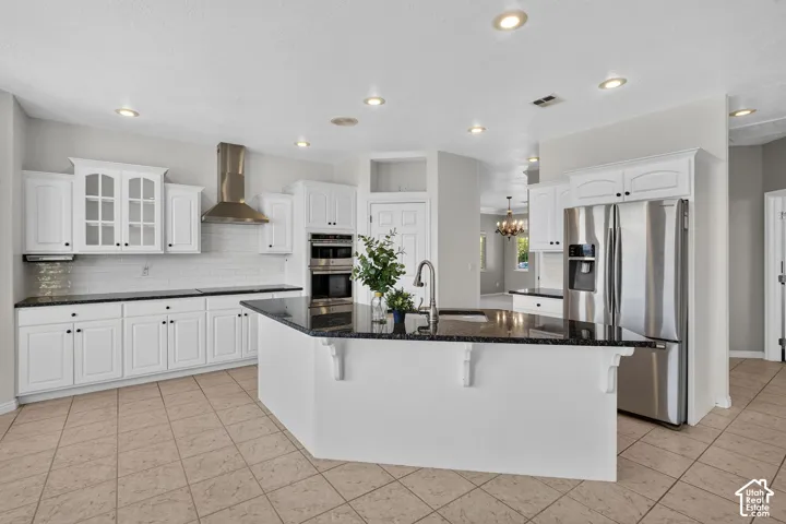 Chef's kitchen featuring white cabinetry with glass-front uppers, stainless steel appliances including double wall ovens and a professional-style range hood, quartz countertops, a large center island with seating, recessed ceiling lighting, and tile floor