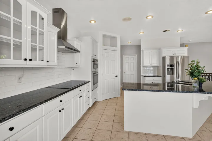 White cabinetry, dark countertops, tile flooring, stainless steel appliances, and recessed lighting