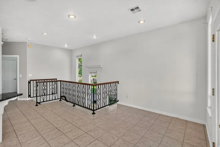 Tiled flooring, wrought iron railing with wood-finish top, recessed lighting, and a white interior door