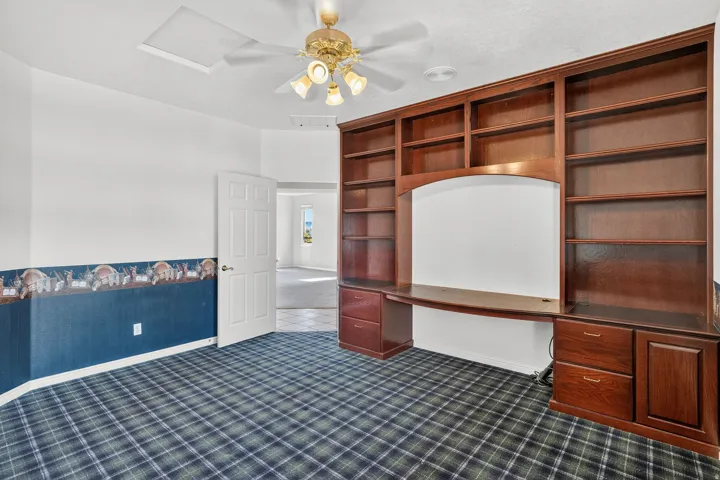 Spacious recreation room featuring built-in wood cabinetry with display shelving, a large whiteboard inset, and plaid carpet flooring