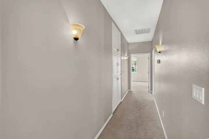 Bright hallway featuring neutral wall finishes, recessed ceiling lighting, carpet flooring, and multiple white interior doors with polished hardware