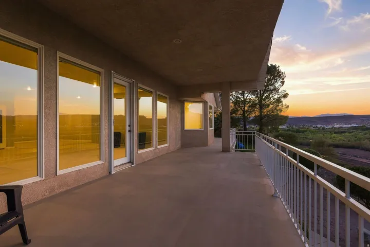 Expansive balcony with a smooth concrete surface, multiple large windows, and a white metal railing
